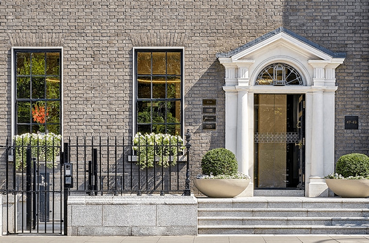 A Georgian building with an ornate white door and tall leaded windows with a black iron fence and bushes outside.