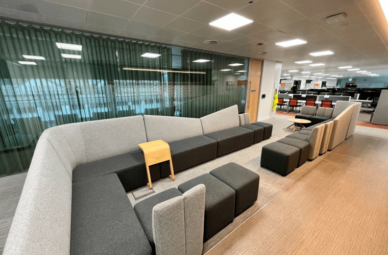 An open plan seating area with sofas in front of a meeting room.