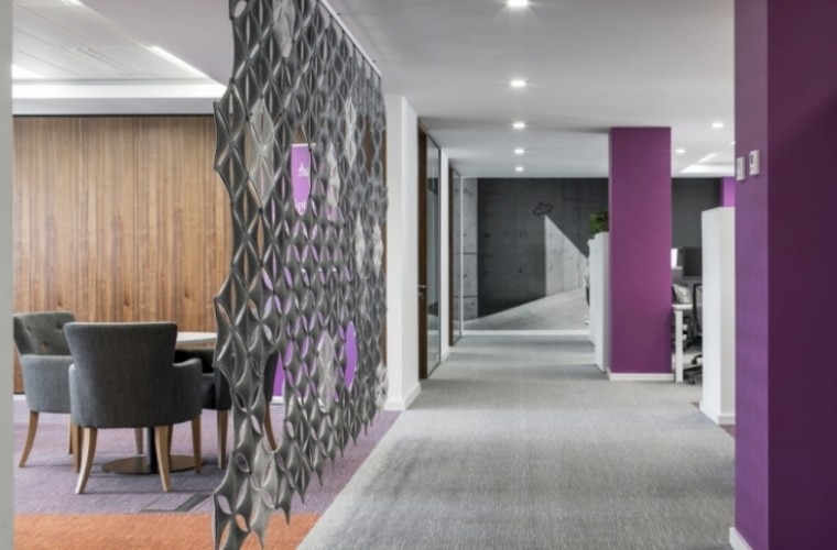 An office space with purple pillars, desks and casual seating.