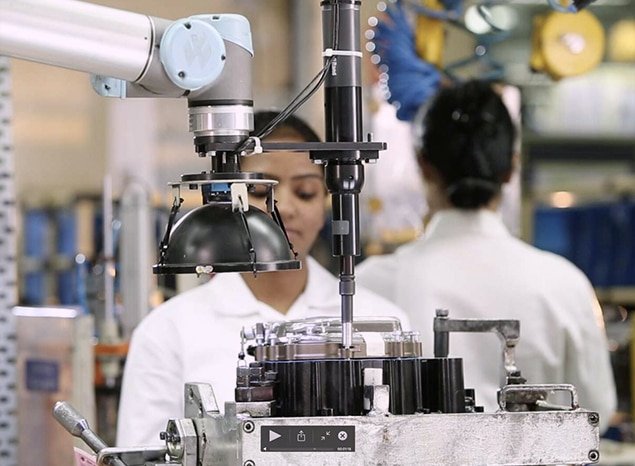 A cobot helps a woman perform her job at an automotive company.