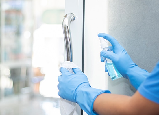 Closeup of hands in protective gloves spraying disinfectant on door handle