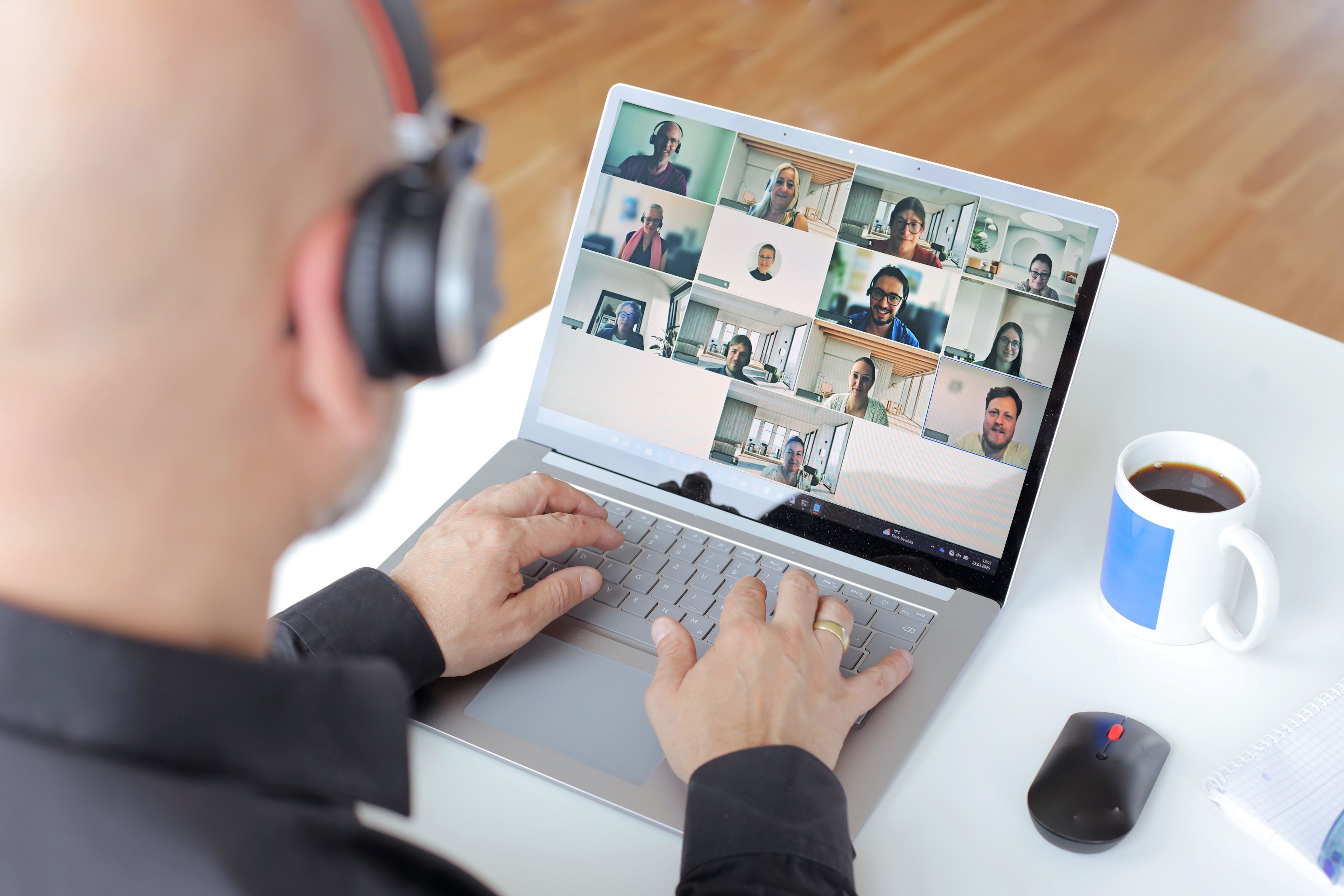 Blick von hinten auf einen Kollegen. Der Kollege hat ein Headset auf und sitzt an einem Laptop. Er ist in einem Teams-Meeting.