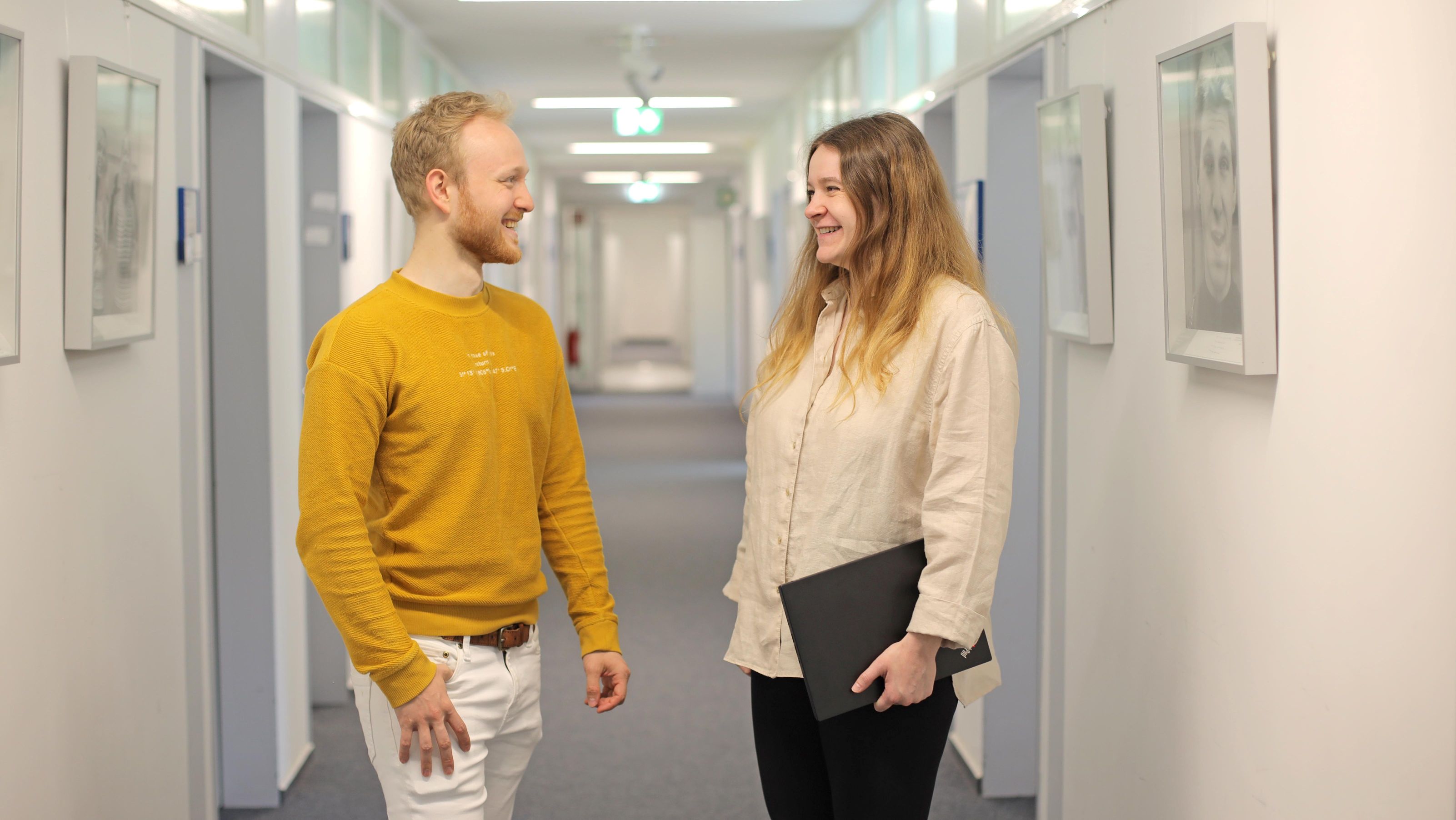 Ein Kollege und eine Kollegin stehend lachend im Flur und unterhalten sich.