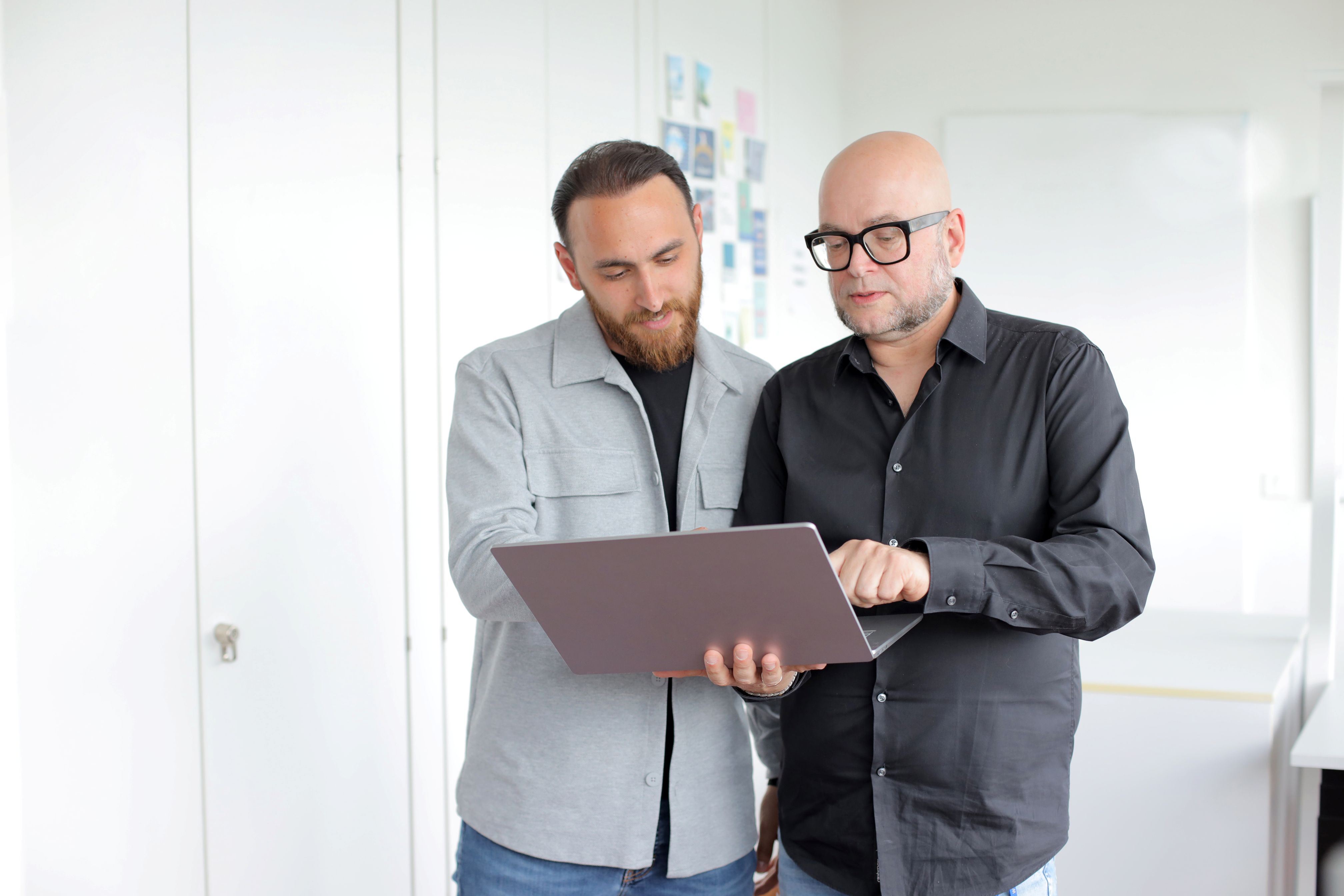 Zwei Kollegen stehen im Büro und schauen gemeinsam auf einen Laptop