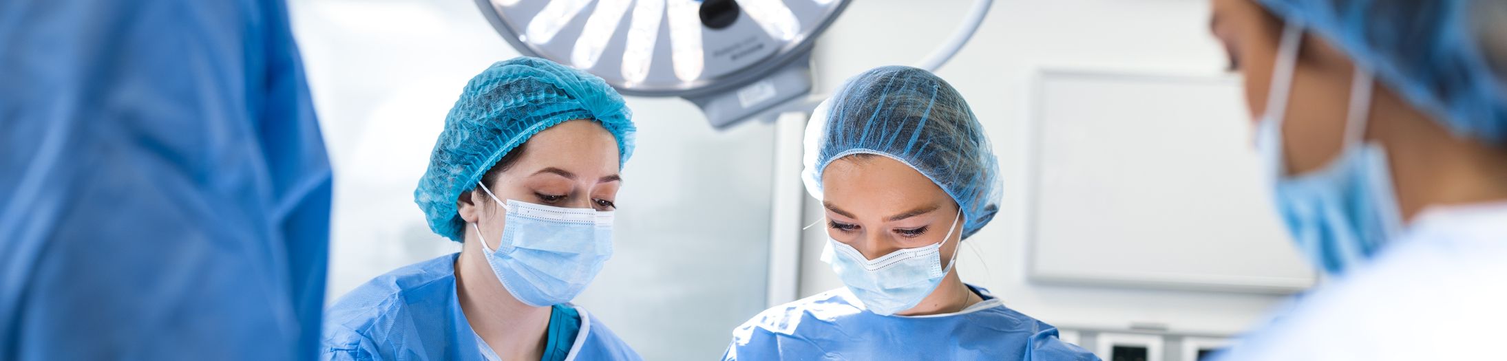 Medical team in surgical attire preparing for a procedure under an operating light.