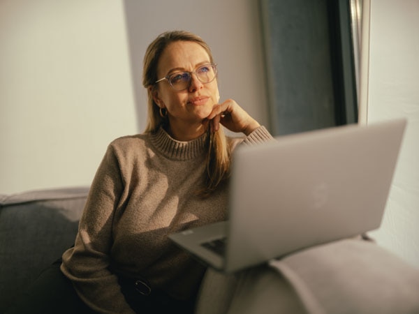 Frau mit Brille sitzt auf Sofa mit Laptop 