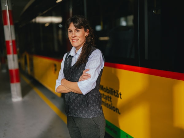 Frau in Uniform vor PostAuto mit Arme verschrenkt