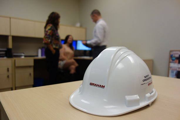 Picture of a hard hat and Graham employees working in the background.