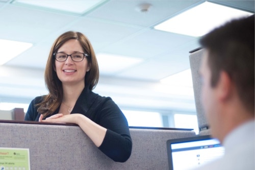Image: A woman leans over a colleague's cubicle to talk, exemplifying the teamwork and collaboration that is at the heart of IESO's culture.