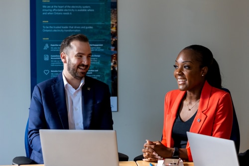 An image of a woman and a man smiling at a table with laptops.