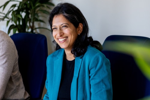 An image of a woman sitting at a table and smiling in an office setting.