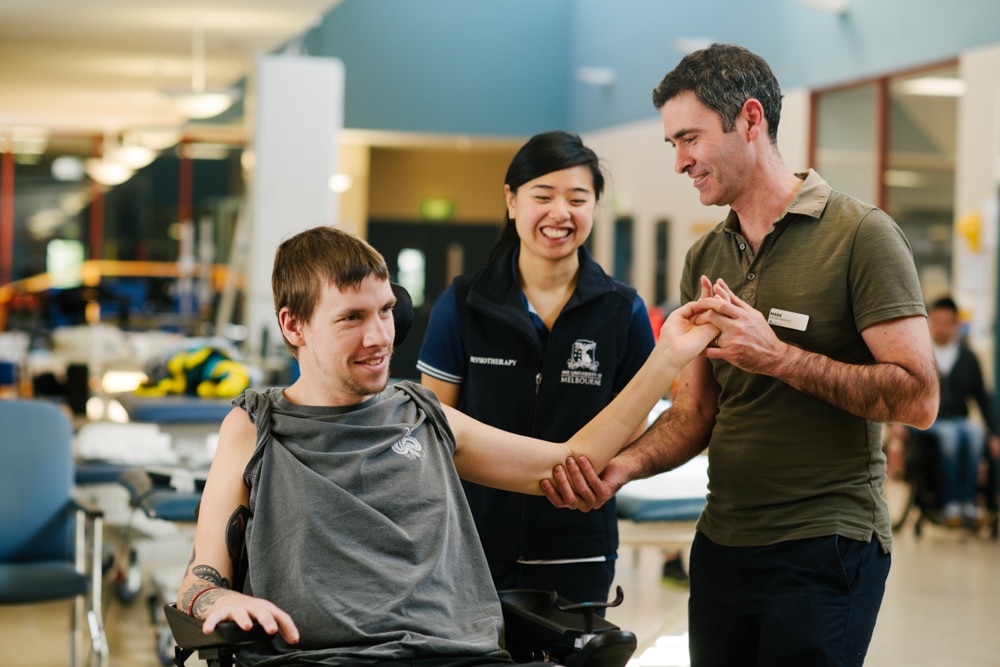 An allied health worker helps a patient with a prosthetic to practice walking