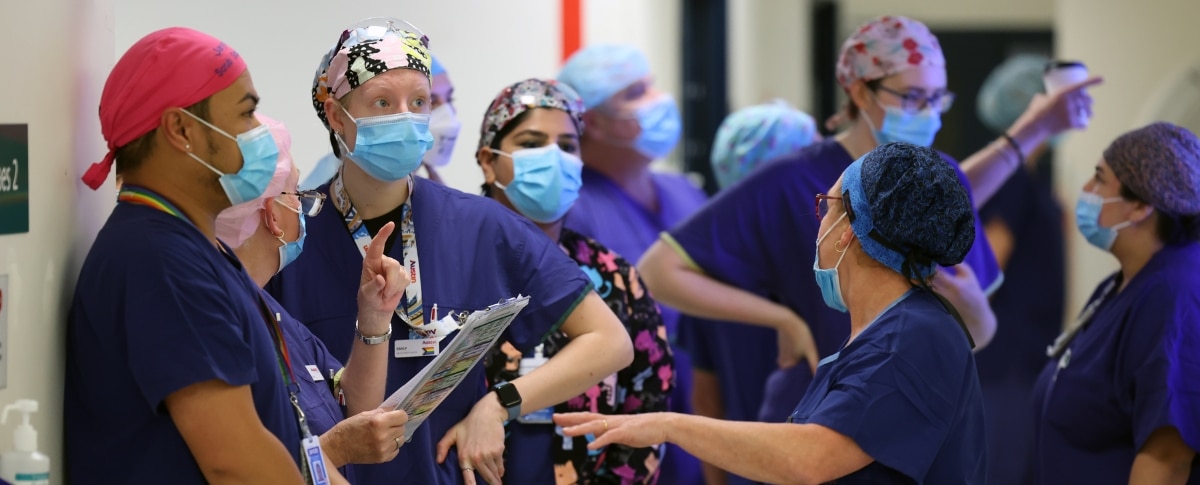 A group of doctors in scrubs and wearing masks having a discussion