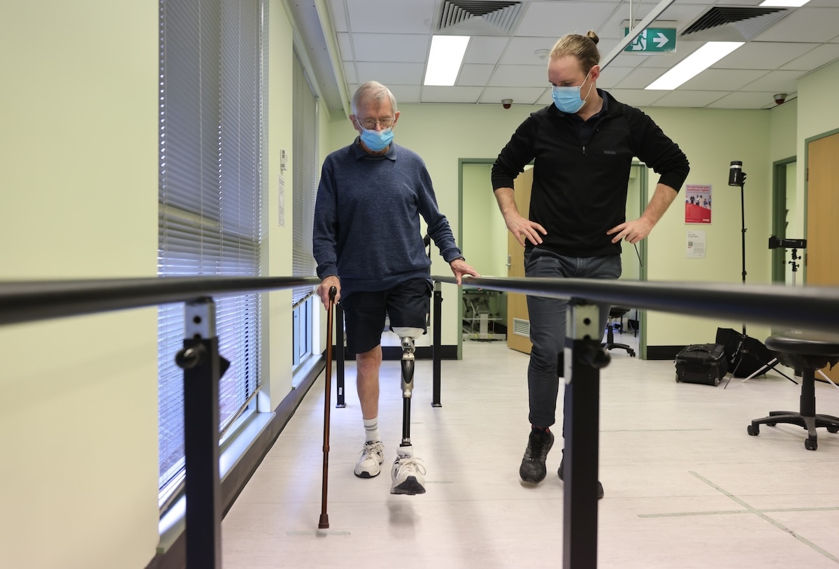 An allied health worker helps a patient with a prosthetic to practice walking
